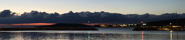 Harbor at dusk with lights blinking in the distance.